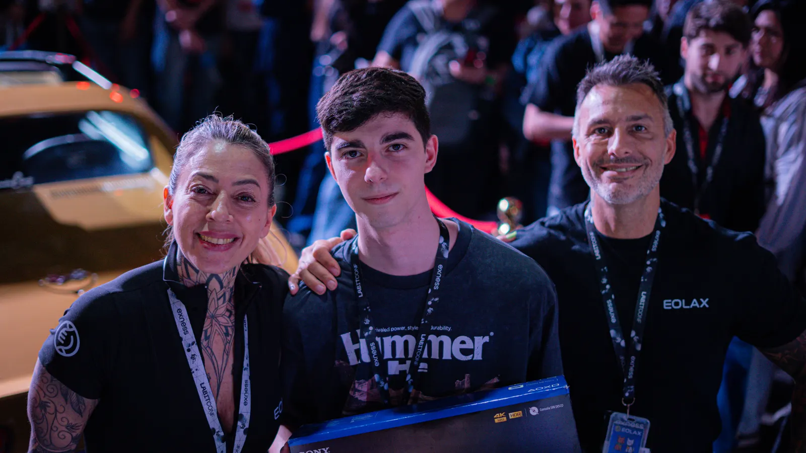 Facu sostiene la caja de la PlayStation 5 entre dos integrantes del equipo de Eolax, con el Corvette detrás.