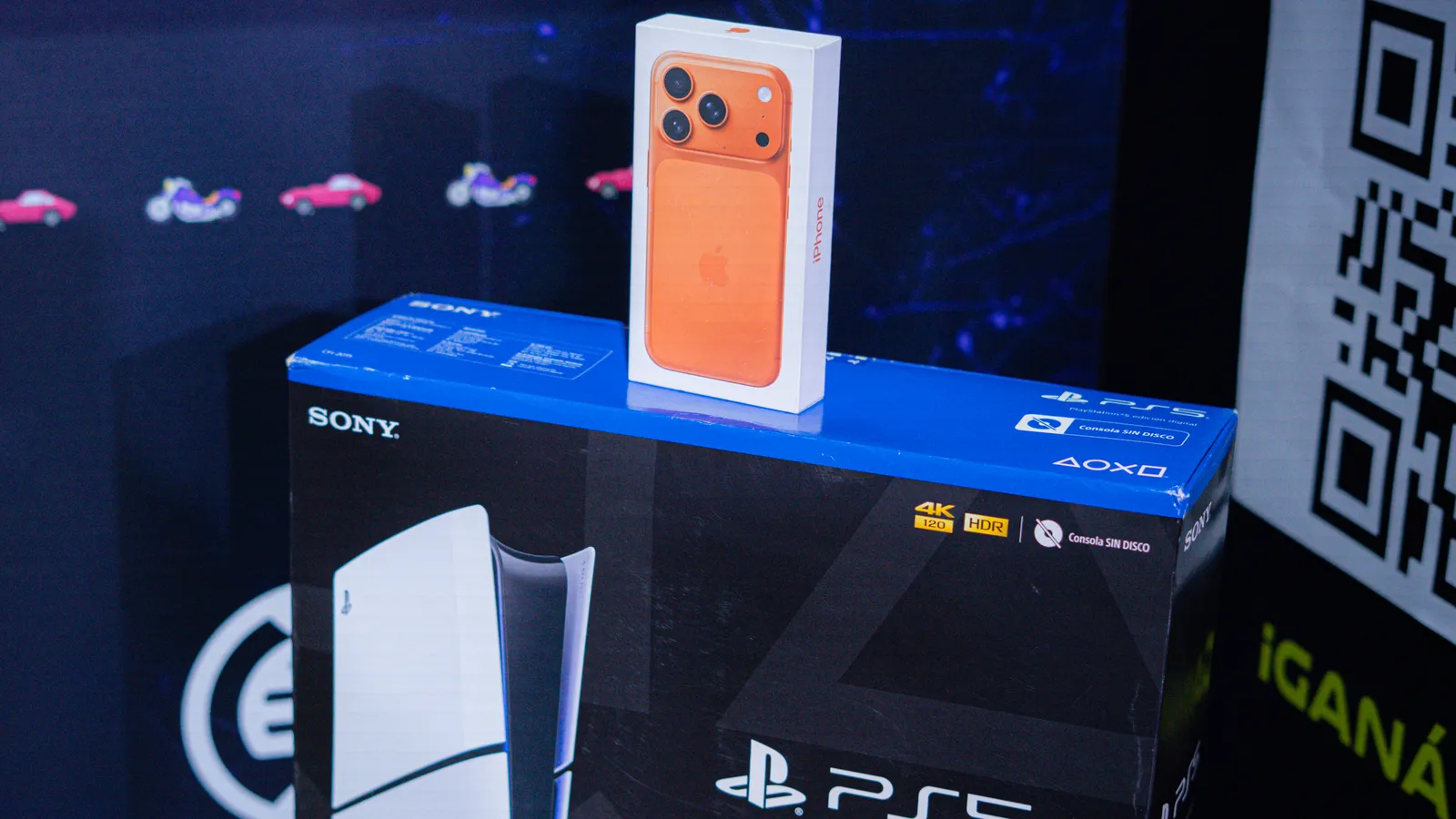 La caja del iPhone 17 Pro naranja apoyada sobre la de la PlayStation 5, en el stand de Eolax, junto al QR para participar.