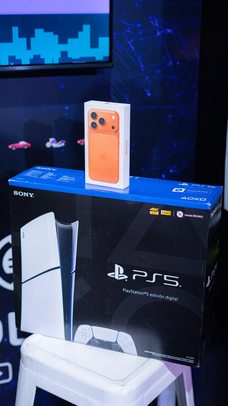 Los premios del stand: una caja de PlayStation 5 edición digital con un iPhone 17 Pro naranja apoyado encima.