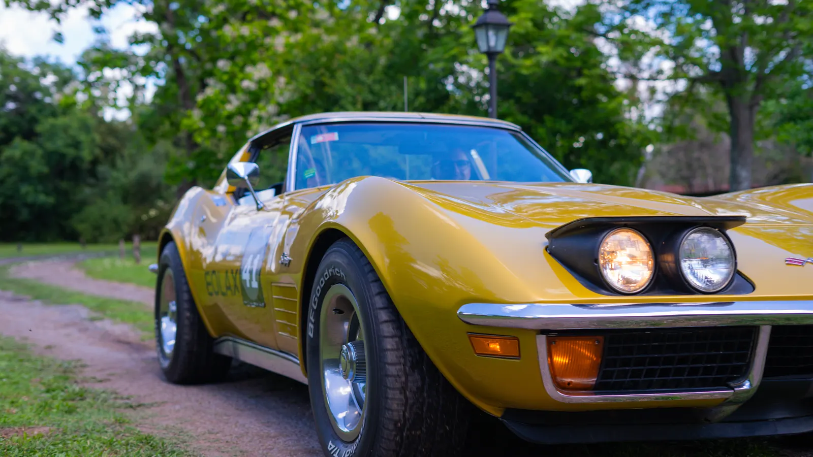 El Corvette Stingray de frente y tres cuartos, con los faros encendidos, detenido sobre el camino de tierra.