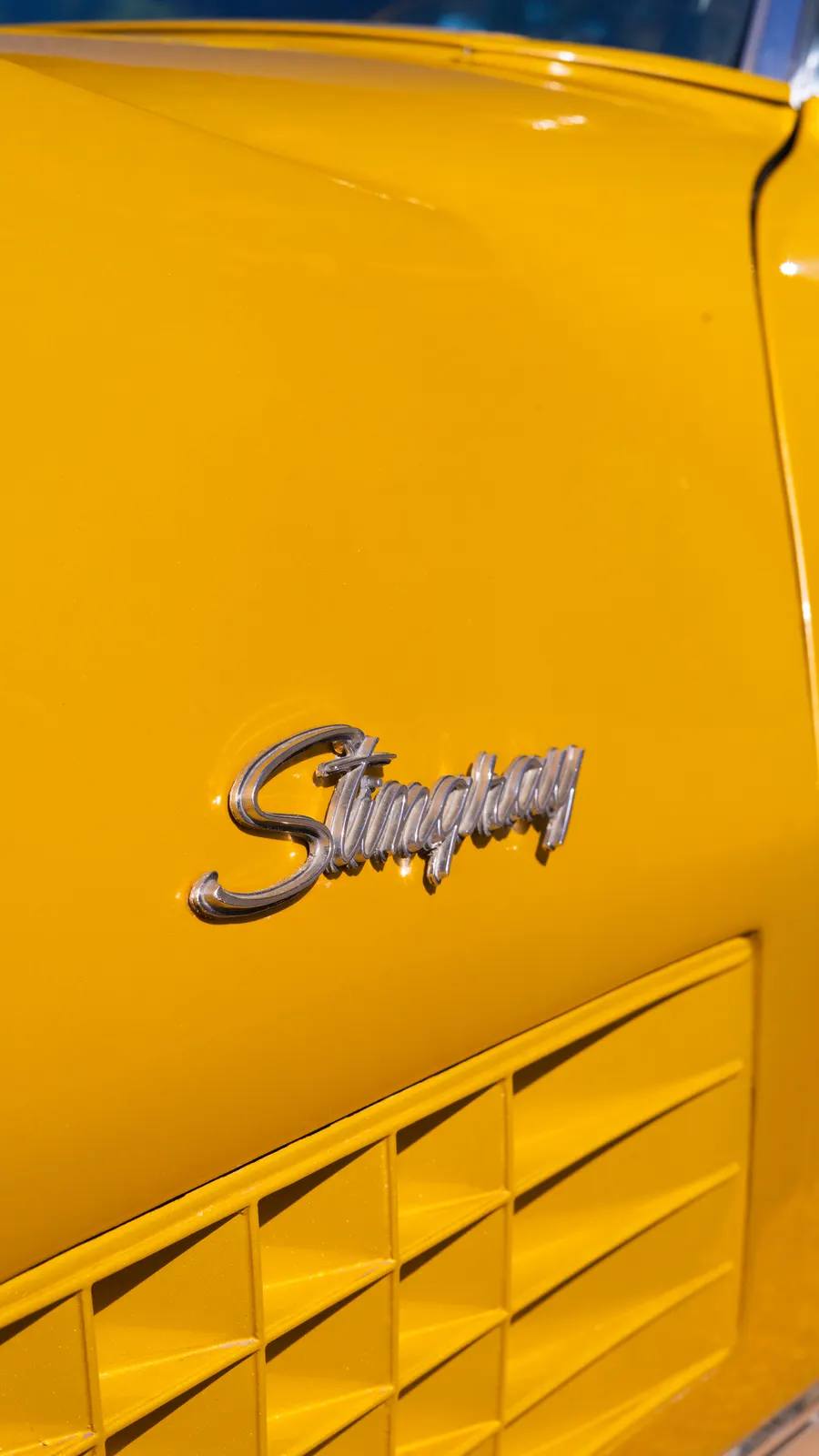 El emblema cromado Stingray sobre la carrocería dorada del Corvette.