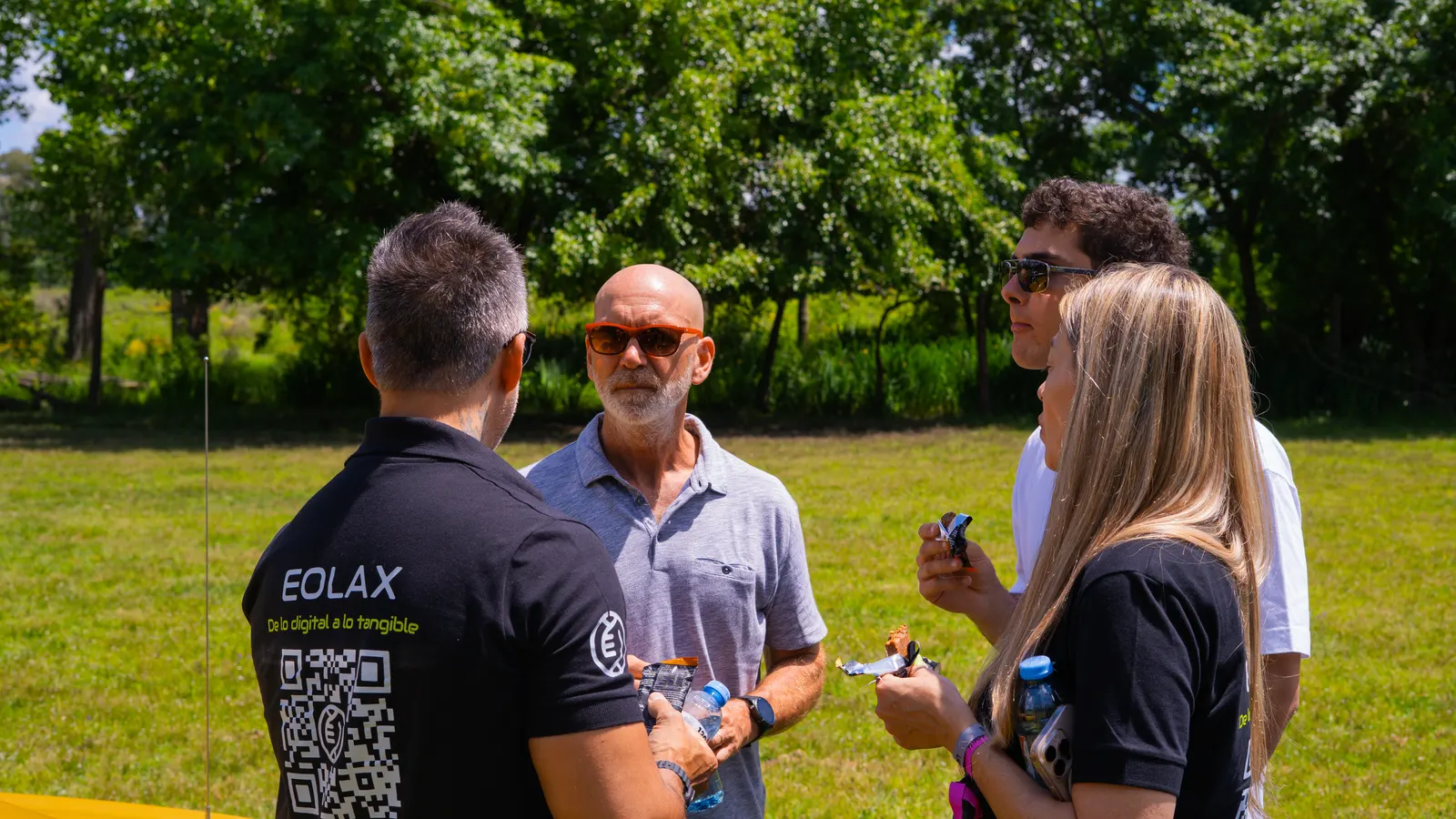 Un integrante del equipo, con el QR de Eolax en la espalda de su remera, conversa con dos asistentes sobre el césped.