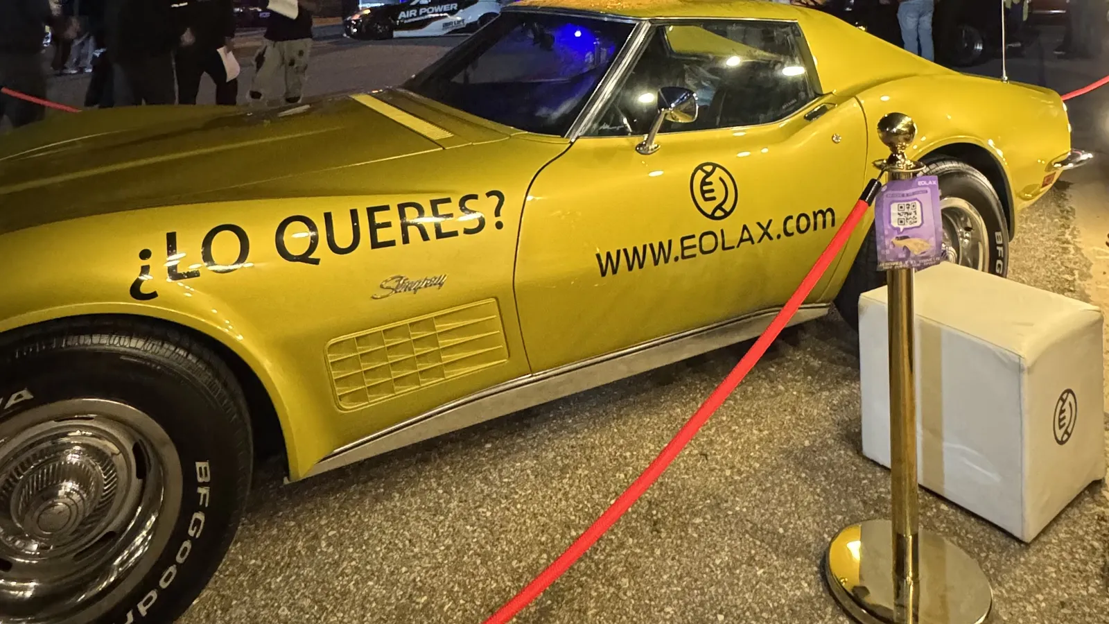 El Corvette Stingray dorado tras la soga roja del circuito, de noche, con «¿LO QUERÉS? WWW.EOLAX.COM» en la puerta.
