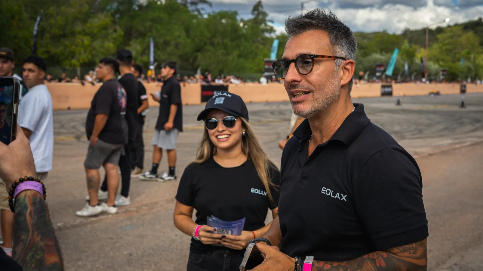 Dos integrantes del equipo de Eolax conversan con una asistente que sostiene su ticket en el paddock.