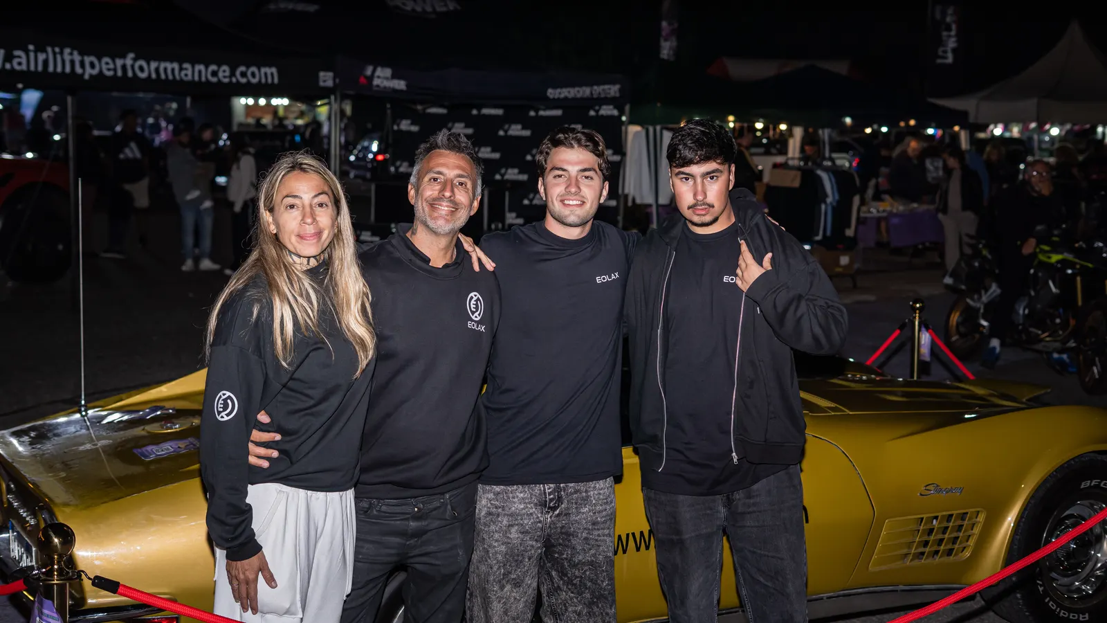 Un grupo posa junto al Corvette dorado en el predio, ya de noche.